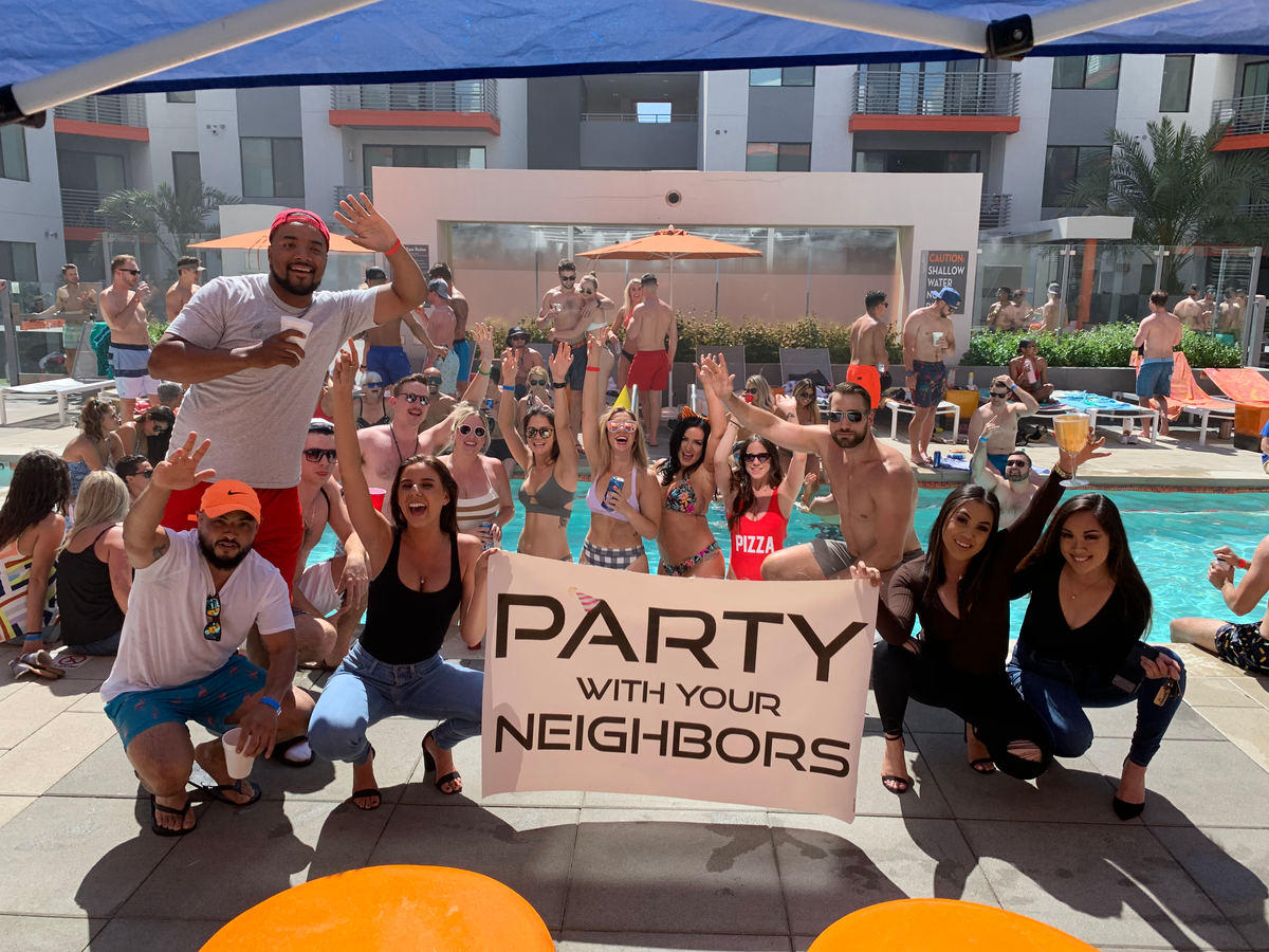 A packed pool deck of residents holding a Party With Your Neighbors sign